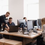 A pleasant, bright, modern office space under daylight with midwest professionals cooperating smoothly on laptops